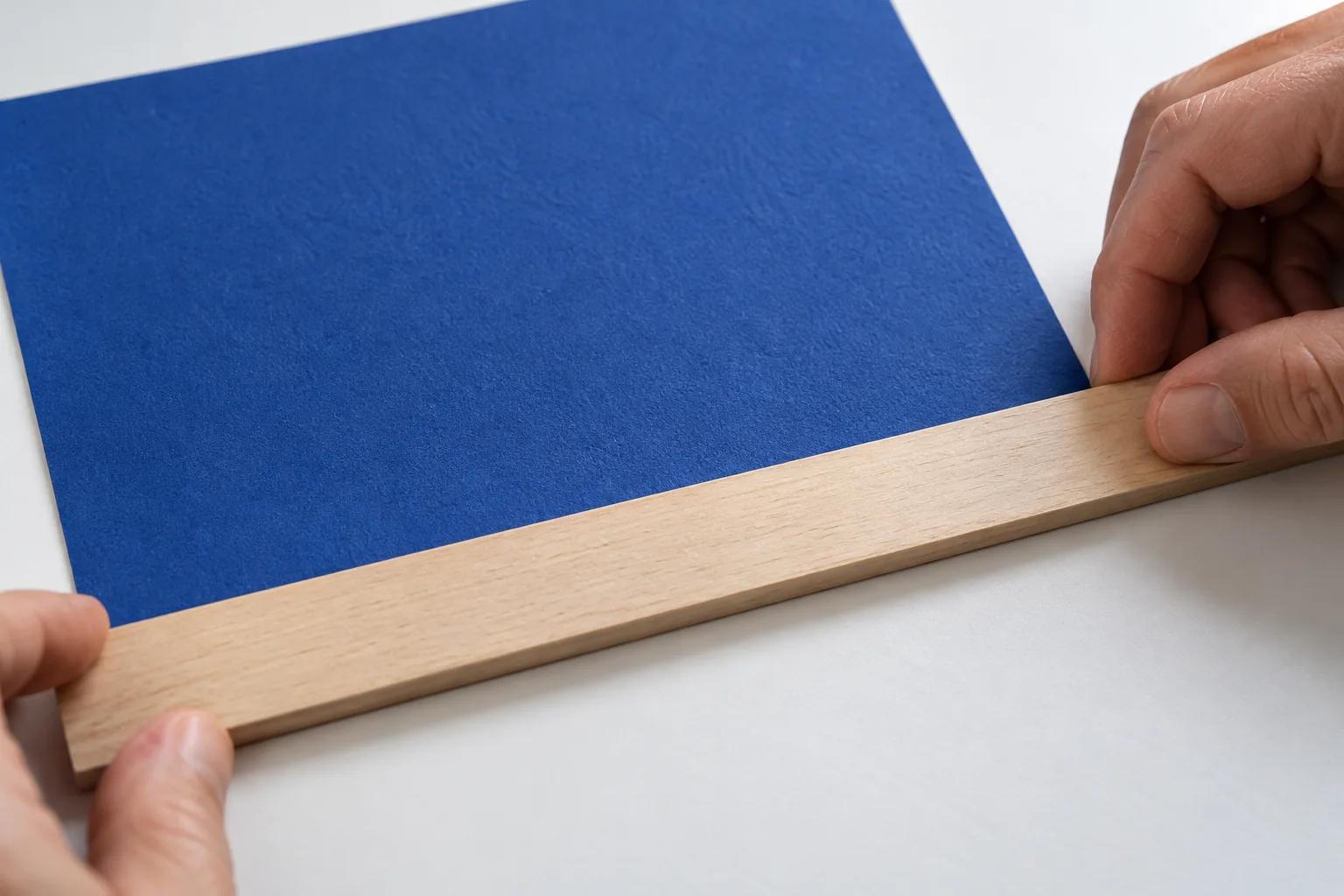 An adult hand uses a plain straightedge to compare the width of a blue paper rectangle
