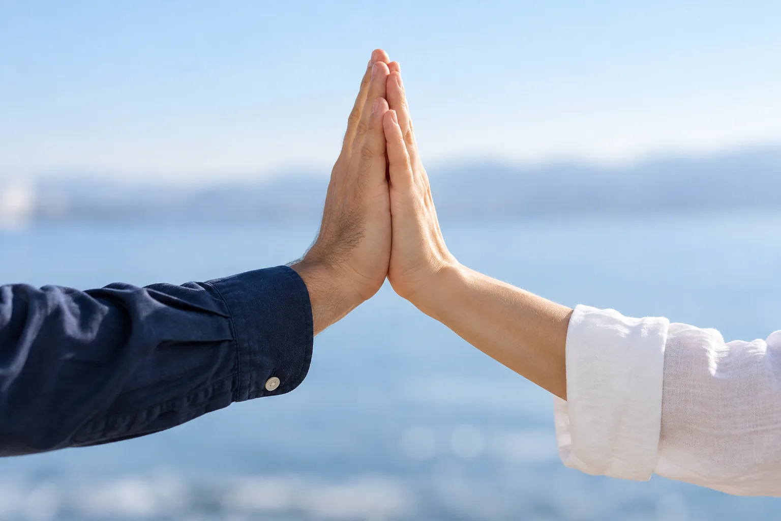 Two adult hands in navy and white sleeves meet palm to palm against a pale blue background